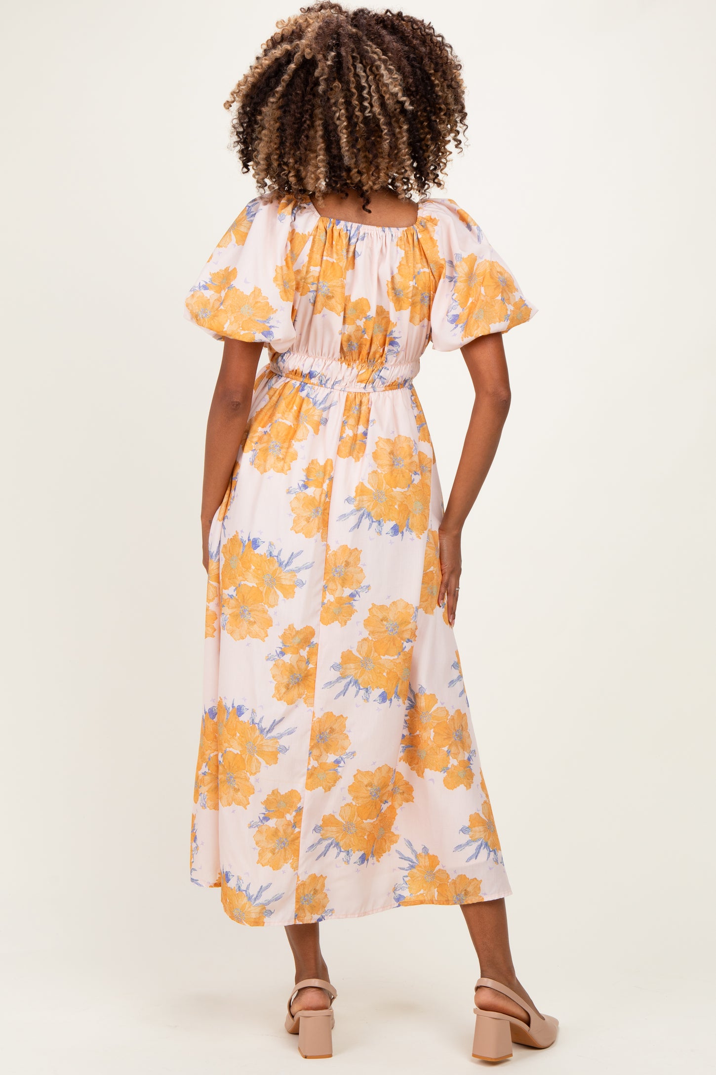 woman wearing a floral maternity maxi dress with puff sleeves and a gathered waist, showing her baby bump from the back