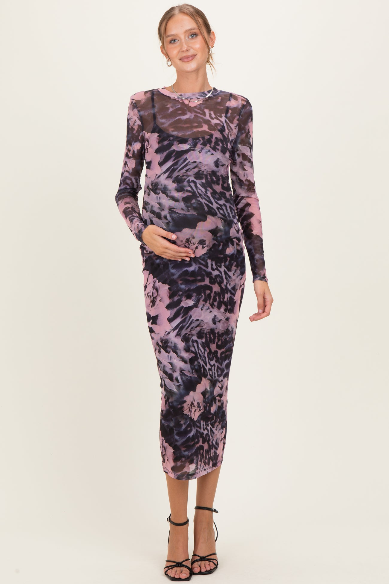 woman wearing a purple and black animal print maternity dress, holding her baby bump, with long sleeves and a fitted silhouette