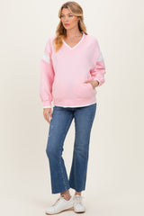 woman wearing a pink maternity sweatshirt with a v-neck and long sleeves, paired with flared jeans and white sneakers