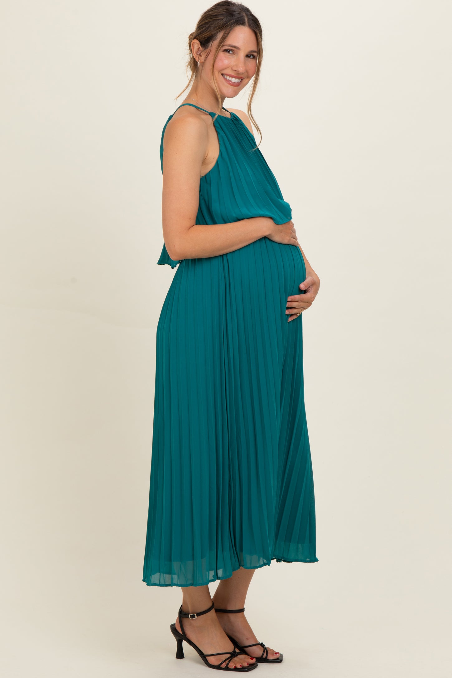 woman wearing a teal pleated maternity dress and gently holding her baby bump