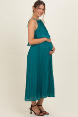 woman wearing a teal pleated maternity dress and gently holding her baby bump