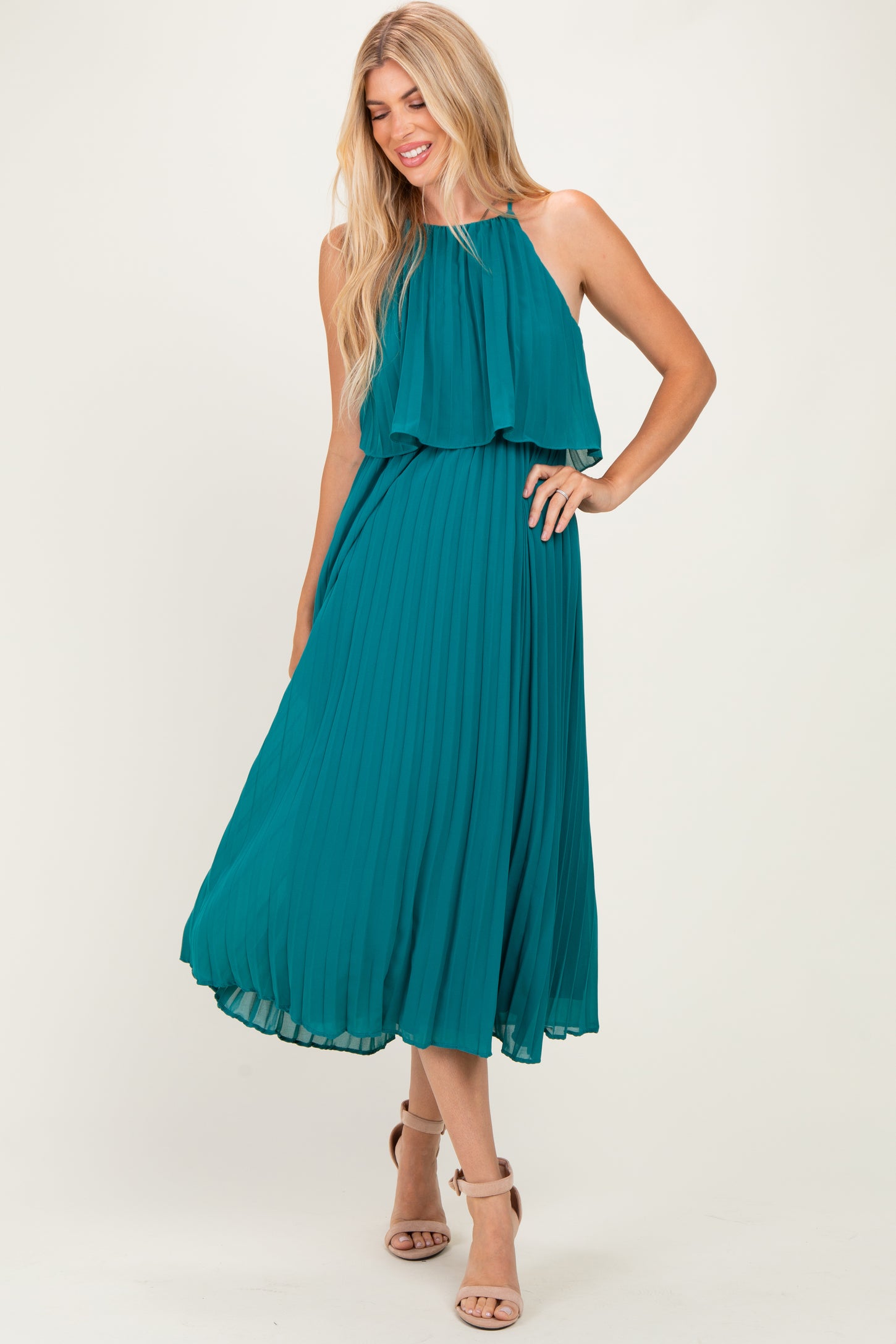 woman wearing a teal sleeveless pleated maxi dress with layered top and strappy heels