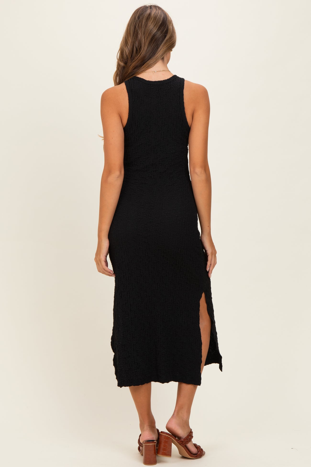 woman wearing a black midi dress with side slits and textured fabric, viewed from the back