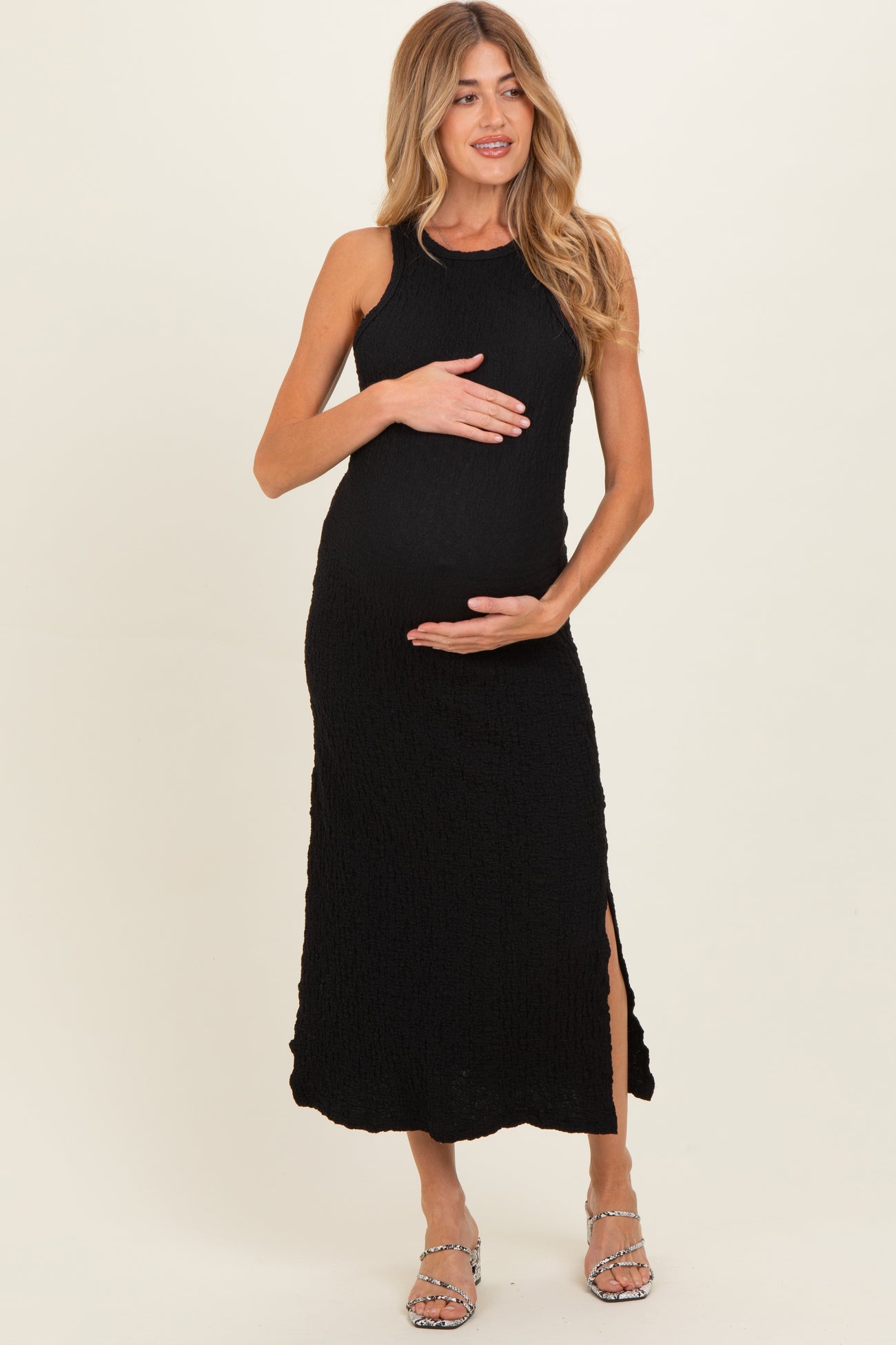 woman wearing a black sleeveless maternity dress with side slits and crinkled texture, holding her baby bump