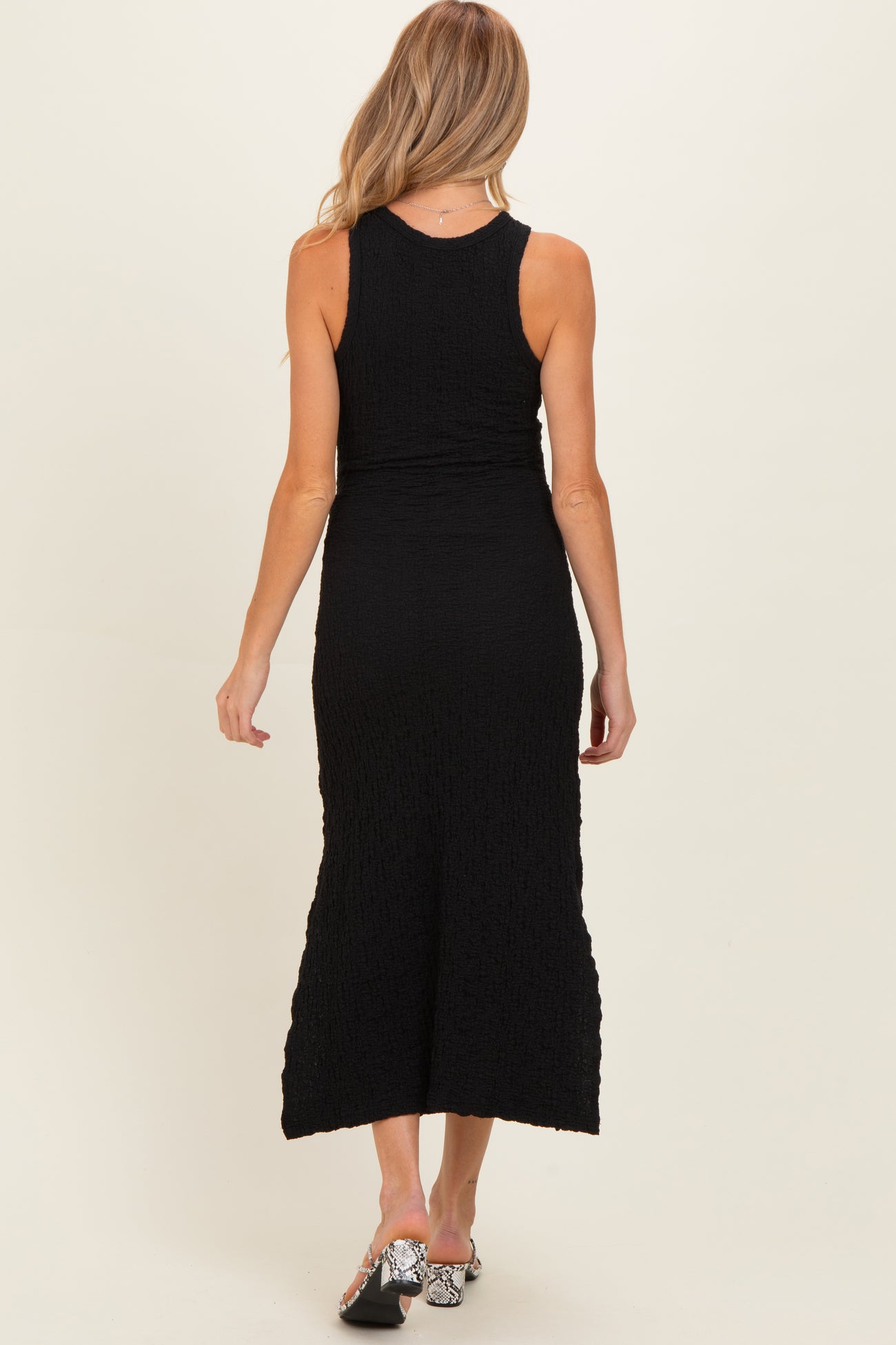 woman wearing a black maternity maxi dress, fitted style with a textured fabric, viewed from the back