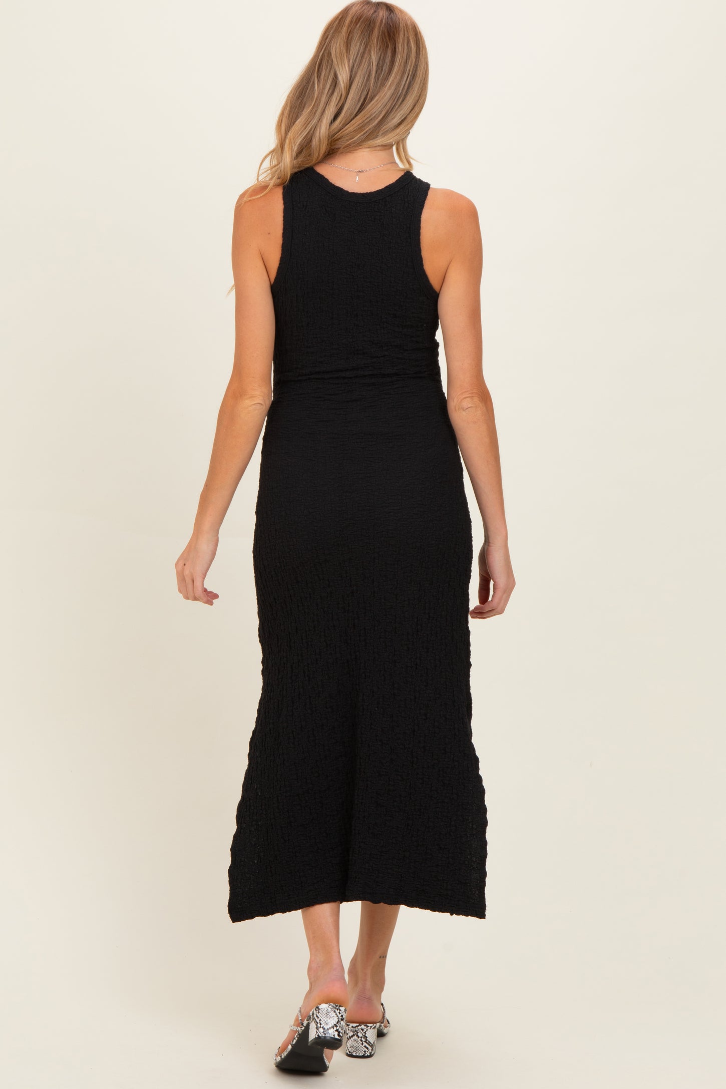 woman wearing a black maternity maxi dress, fitted style with a textured fabric, viewed from the back
