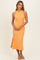 woman wearing a sleeveless orange midi dress with a fitted bodice and side slit, standing against a neutral background