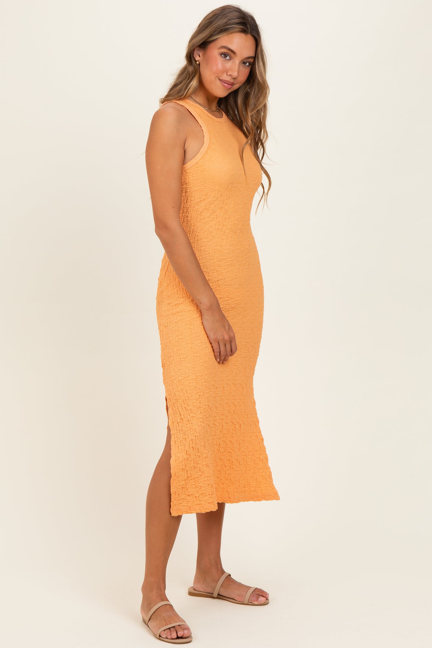 woman wearing a textured orange midi dress with a side slit and sandals