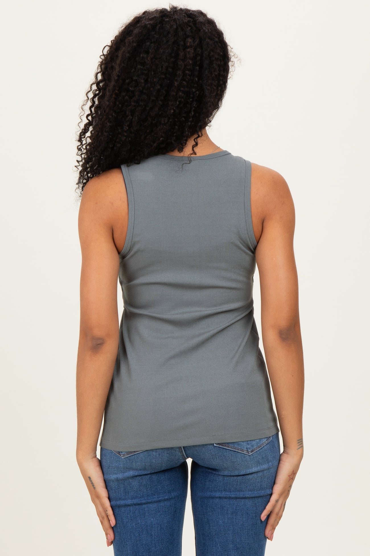 woman wearing a back view of a gray ribbed tank top paired with blue jeans.