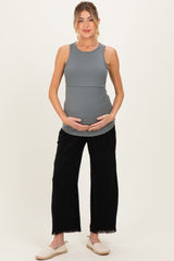 woman wearing a gray maternity tank top and black wide-leg pants, holding her baby bump