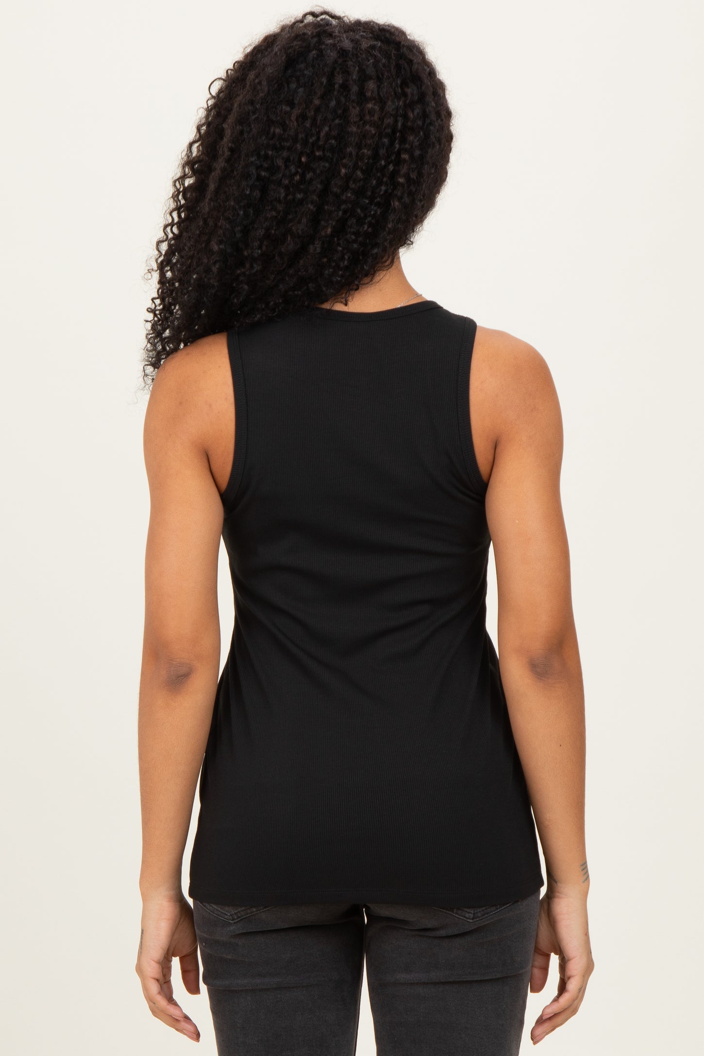 woman wearing a black ribbed tank top, viewed from the back against a neutral background