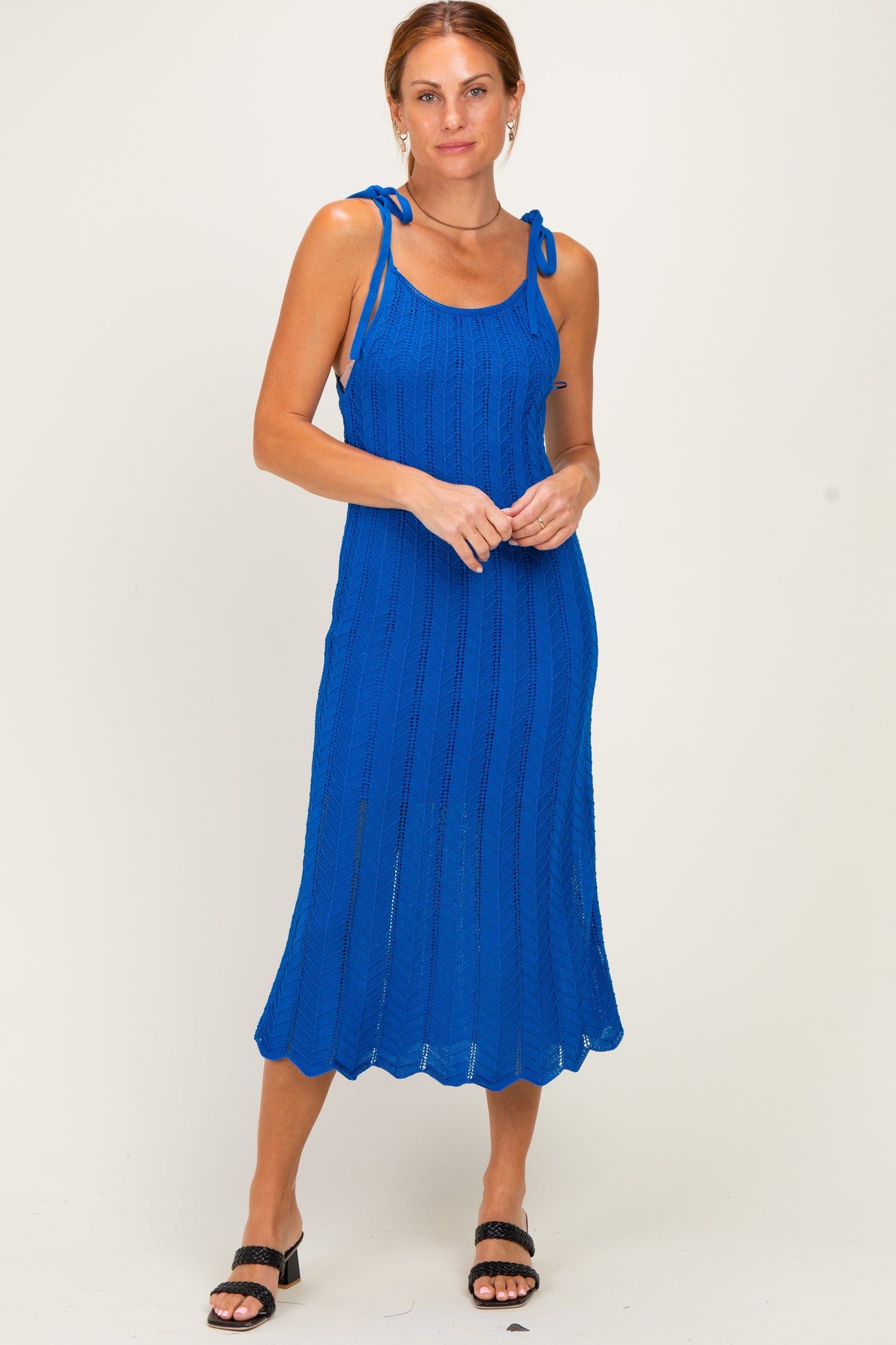 woman wearing a bright blue knit midi dress with tie-straps and a relaxed fit, standing with arms crossed