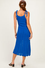 woman wearing a back view of a vibrant blue ribbed knit midi dress with adjustable tie straps and a scalloped hem