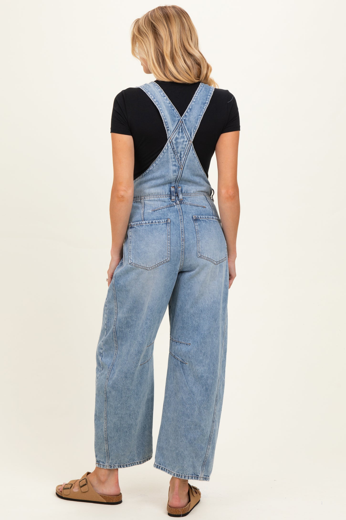 woman wearing light blue maternity overalls with a relaxed fit and cross-back design, showing her baby bump