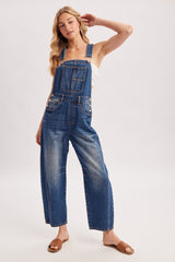woman wearing blue denim overalls with wide legs and adjustable straps, styled with a white tank top and sandals