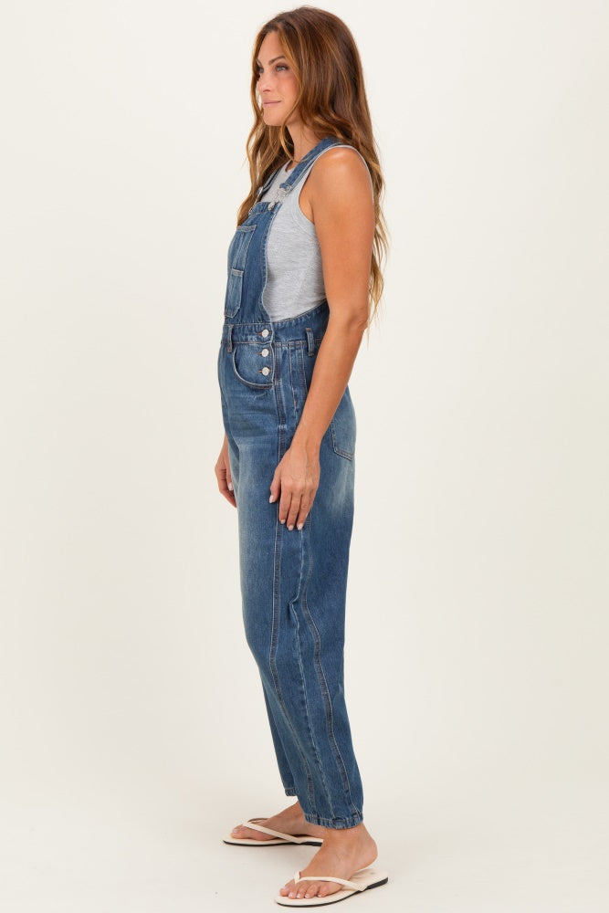 woman wearing a gray tank top under denim overalls with a relaxed fit and side buttons, standing sideways