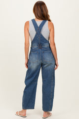 woman wearing a gray tank top and blue denim overalls viewed from the back