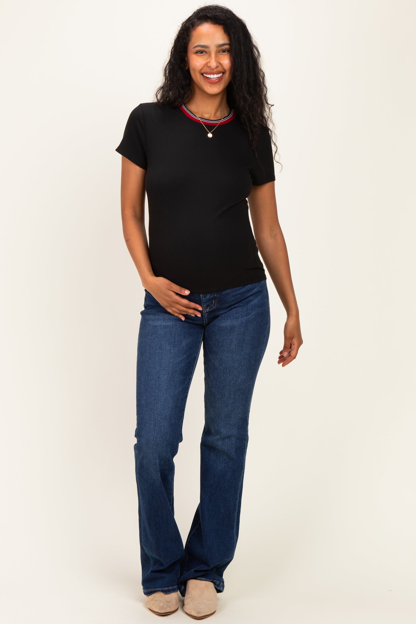 woman wearing a black short sleeve maternity top and blue flared jeans, lightly holding her baby bump