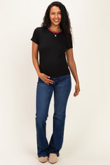 woman wearing a black short sleeve maternity top and blue flared jeans, lightly holding her baby bump