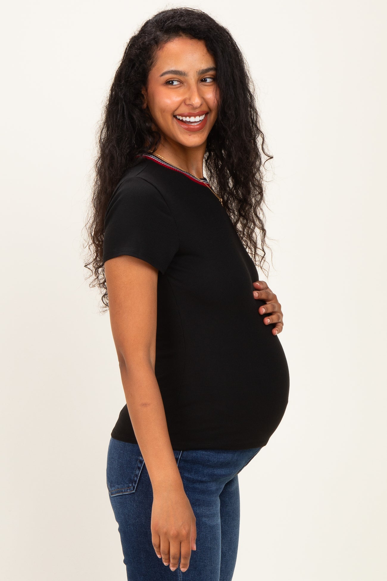 woman wearing a black maternity top with a colorful neckline and showing off her baby bump while smiling