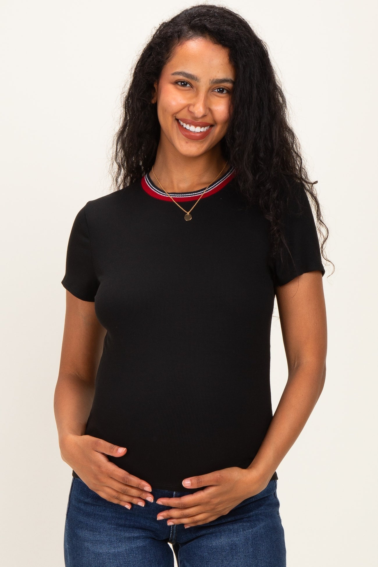 woman wearing a black short sleeve maternity top with a red and white striped neckline and holding her baby bump