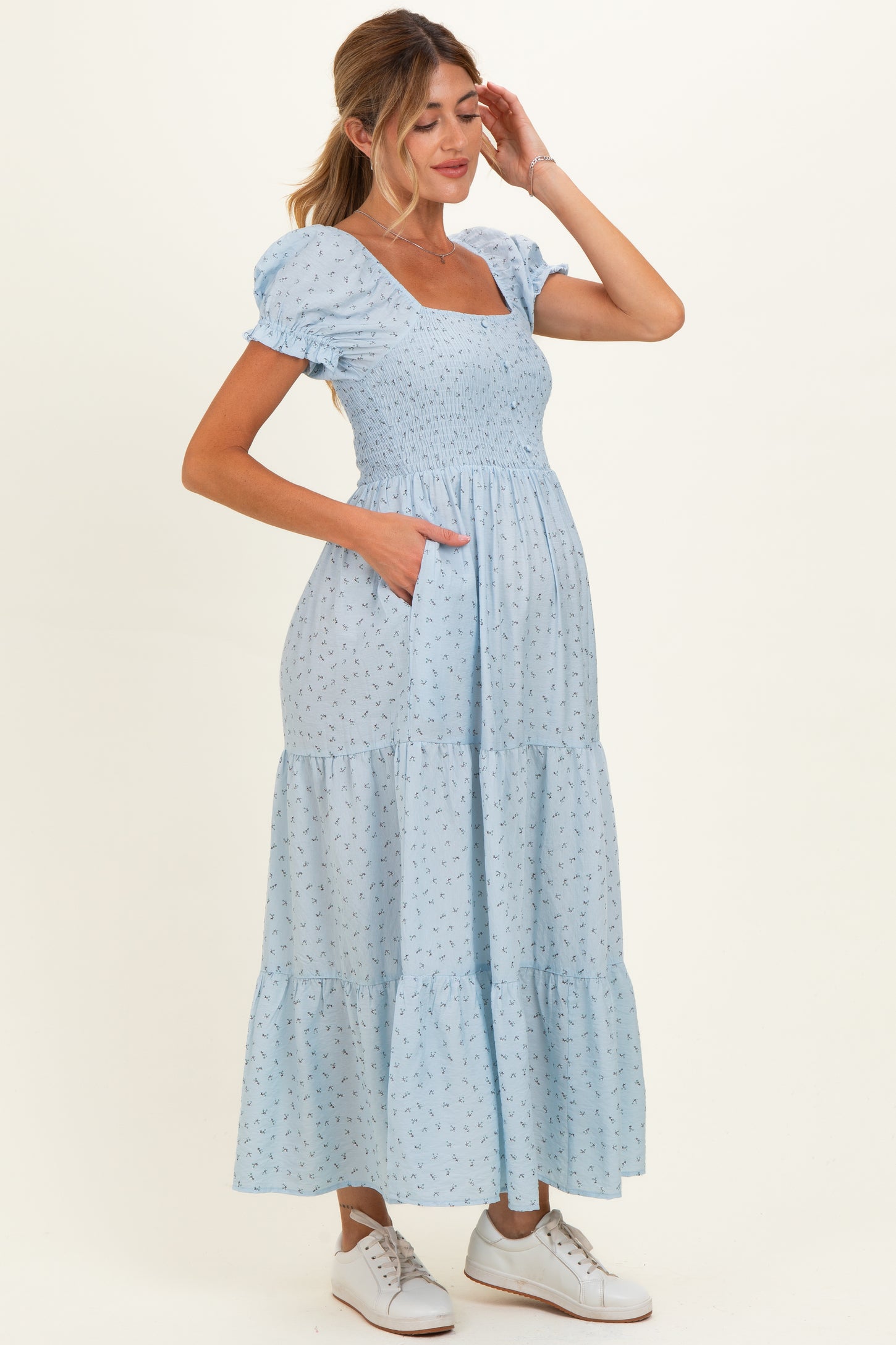 woman wearing a light blue maternity dress with puff sleeves and a tiered skirt, showing a baby bump and pocket details