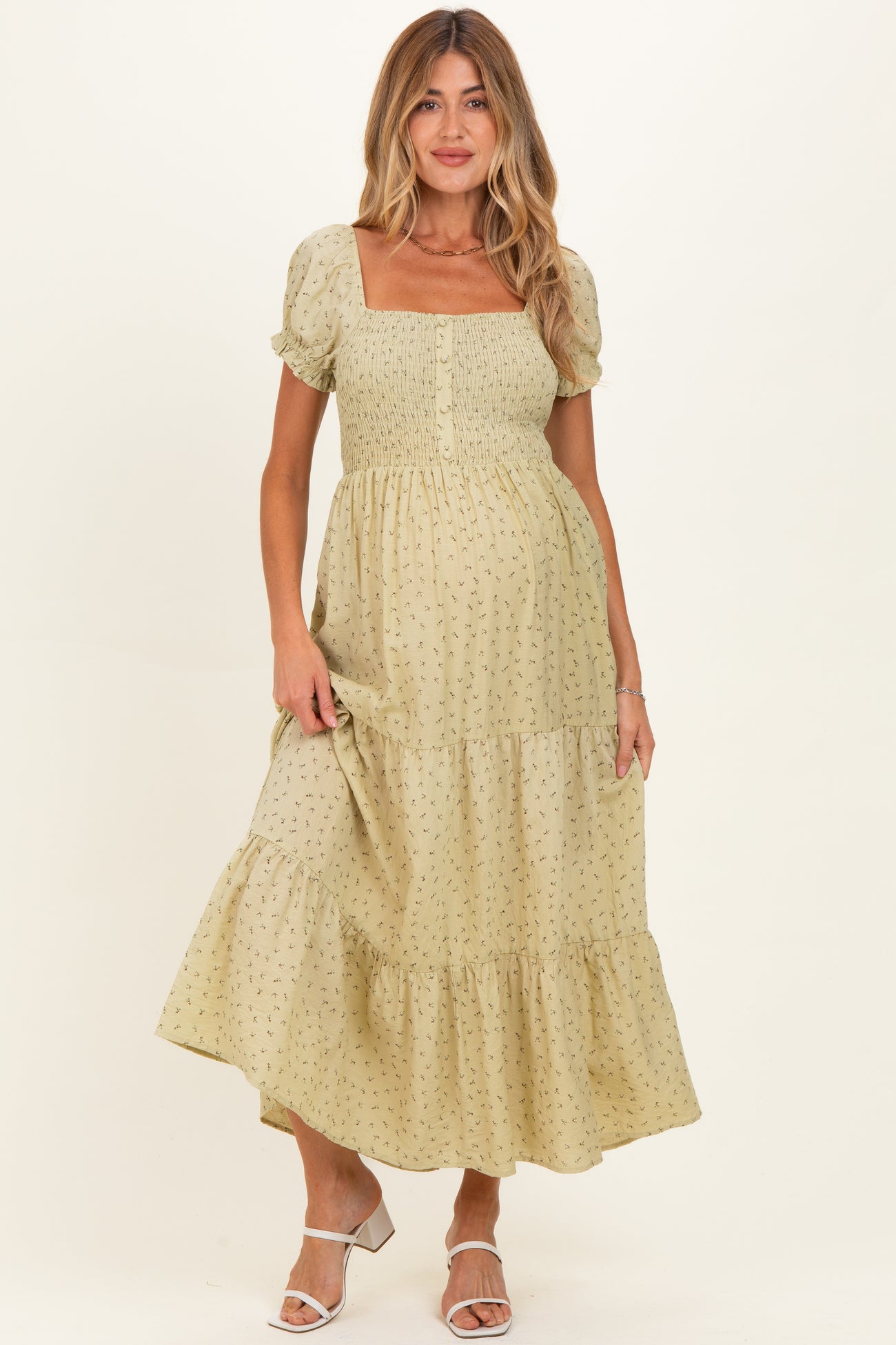 woman wearing a light green floral print maternity dress with a square neckline and puff sleeves, holding her baby bump