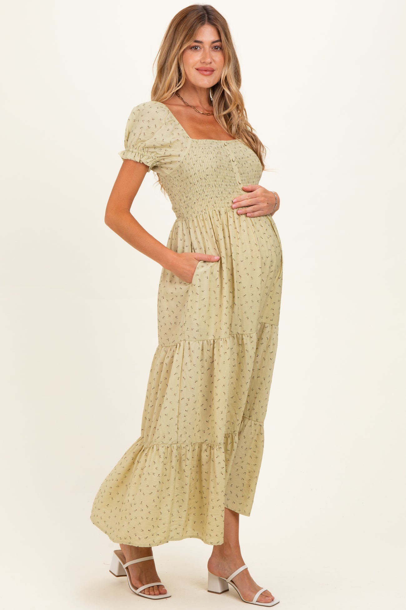 woman wearing a light green floral maternity maxi dress with a smocked bodice and pockets, showing her baby bump