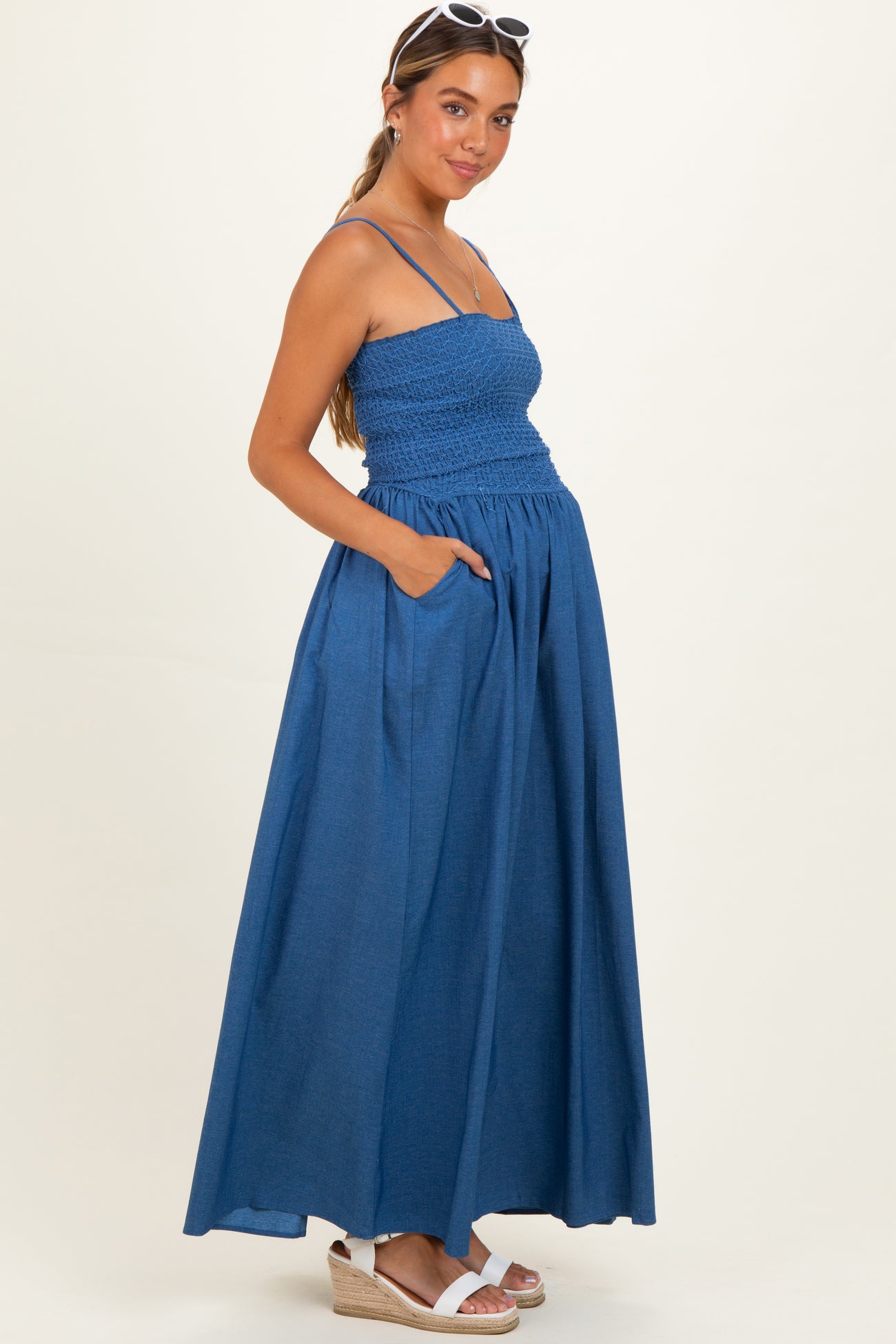 woman wearing a blue maxi maternity dress with smocked bodice and pockets, showing her baby bump