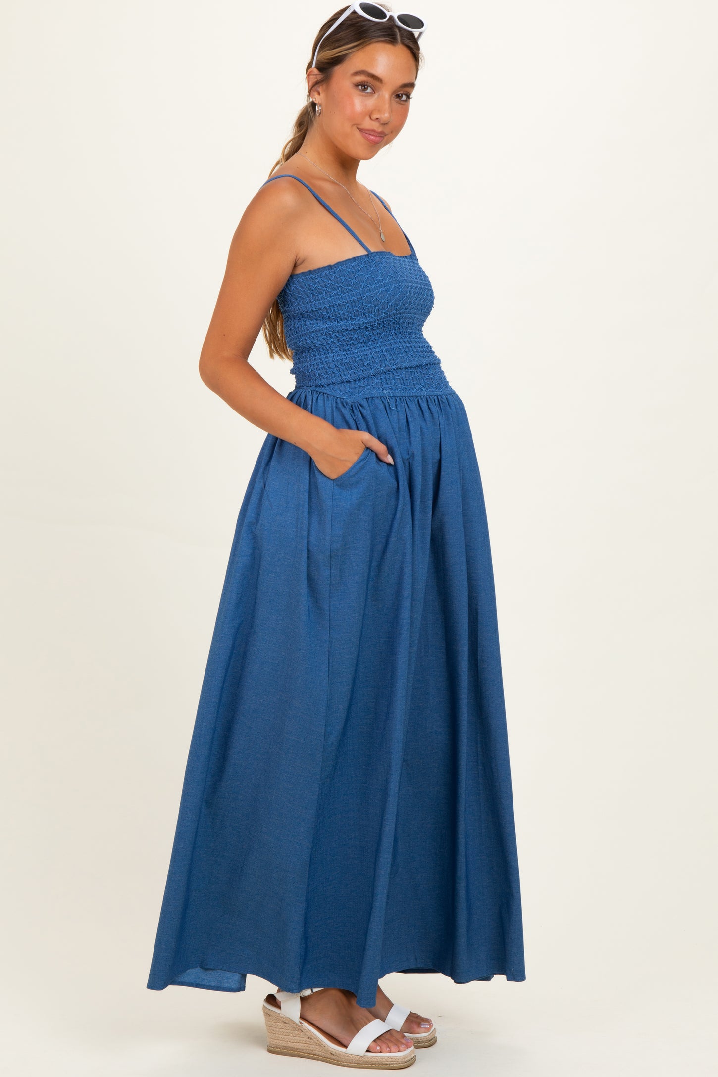 woman wearing a blue maxi maternity dress with smocked bodice and pockets, showing her baby bump