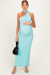 woman wearing a turquoise one-shoulder maternity dress, holding her baby bump and carrying a black handbag