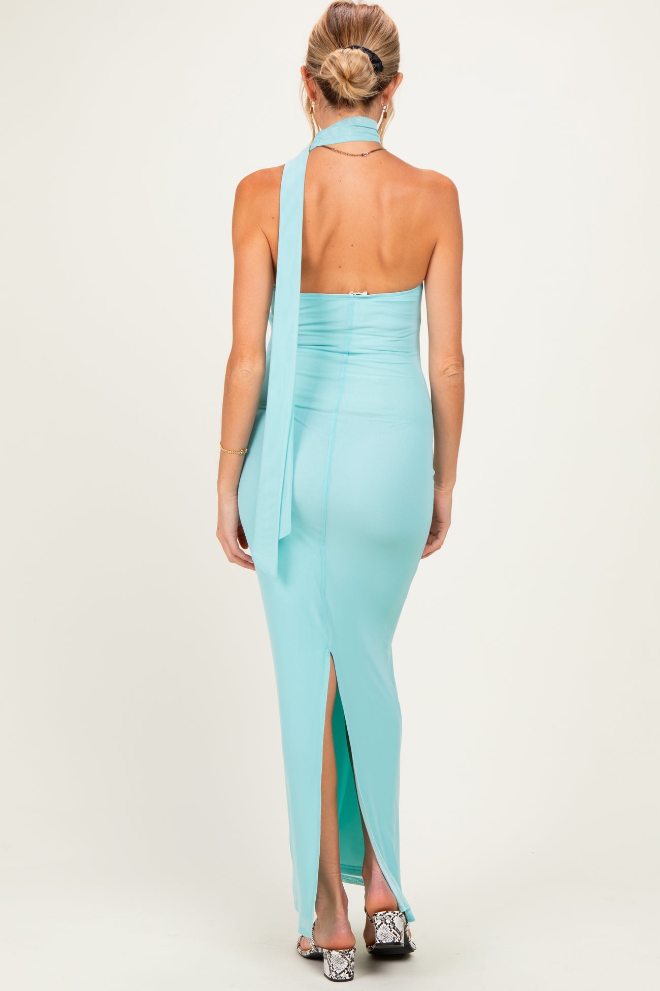 woman wearing a light aqua maternity dress with a halter neckline and a thigh-high slit, showing her back