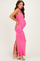 woman wearing a bright pink maternity maxi dress with a halter neck and side slit, showcasing her baby bump