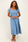 woman wearing a blue midi dress with puff sleeves and floral embroidery, standing against a neutral background