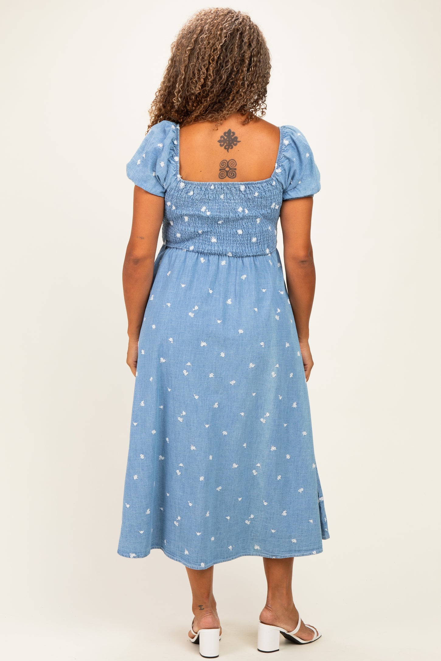 woman wearing a blue denim maxi dress with puff sleeves and a smocked back, standing with a tattoo visible on her back
