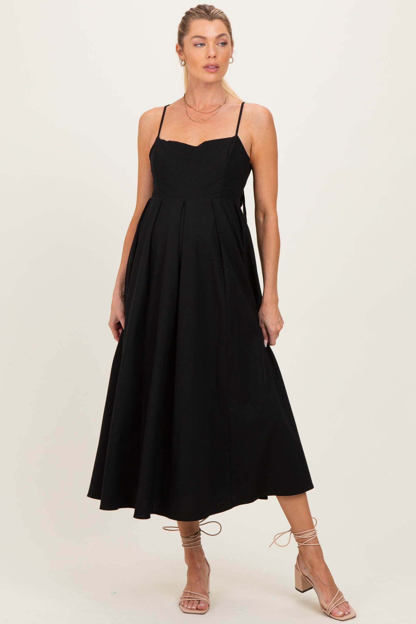 woman wearing a black maternity dress with a sweetheart neckline and pleated skirt, showing her baby bump