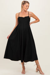 woman wearing a black maternity dress with spaghetti straps and a flowy midi skirt, showcasing her baby bump