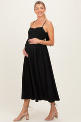 woman wearing a black maternity dress with spaghetti straps and a flowing skirt, holding her baby bump