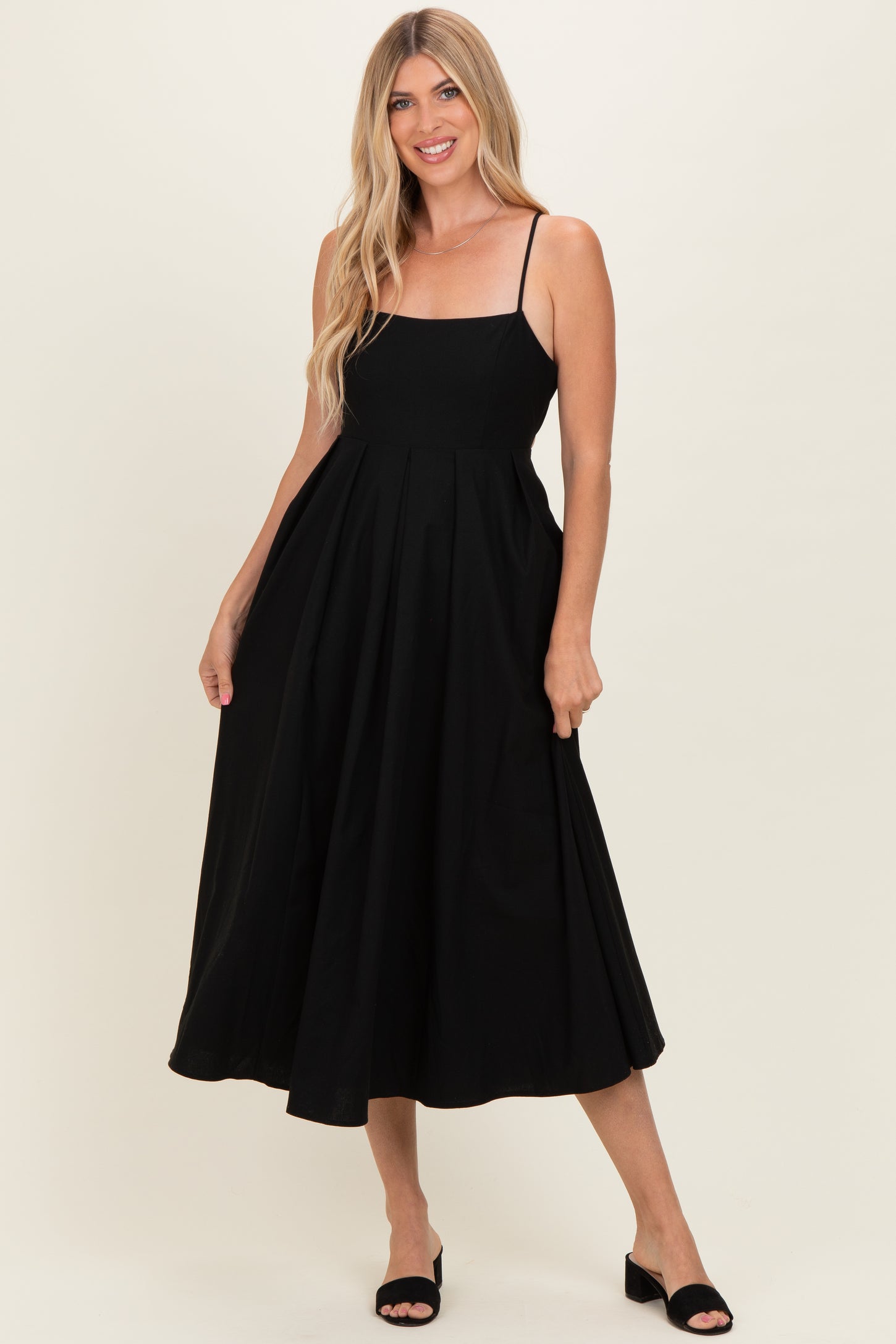 woman wearing a black spaghetti strap midi dress with a fitted bodice and flared skirt