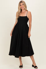 woman wearing a black spaghetti strap midi dress with a fitted bodice and flared skirt