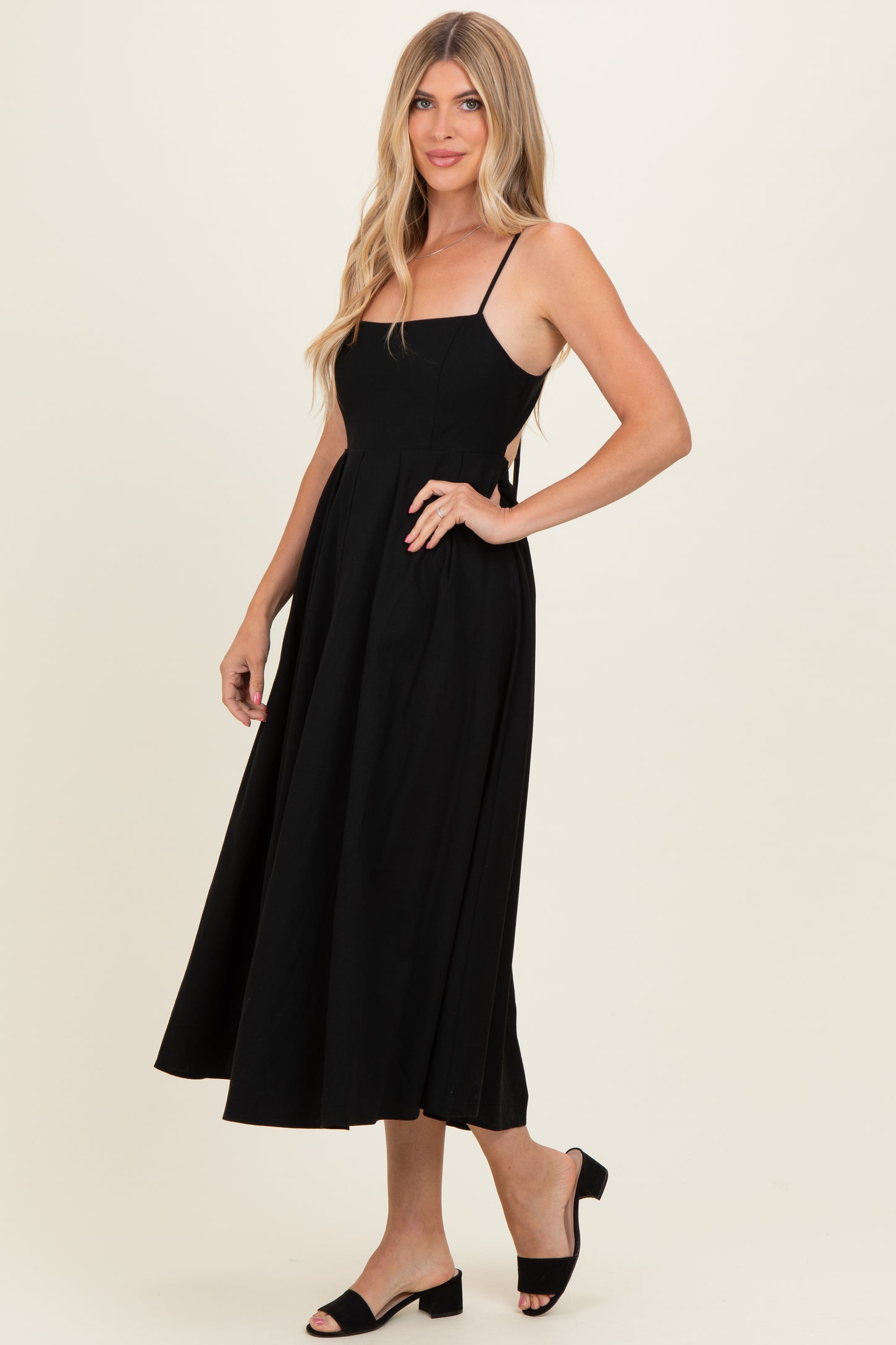 woman wearing a black sleeveless midi dress with a fitted bodice and flowing skirt, styled with black block heel sandals