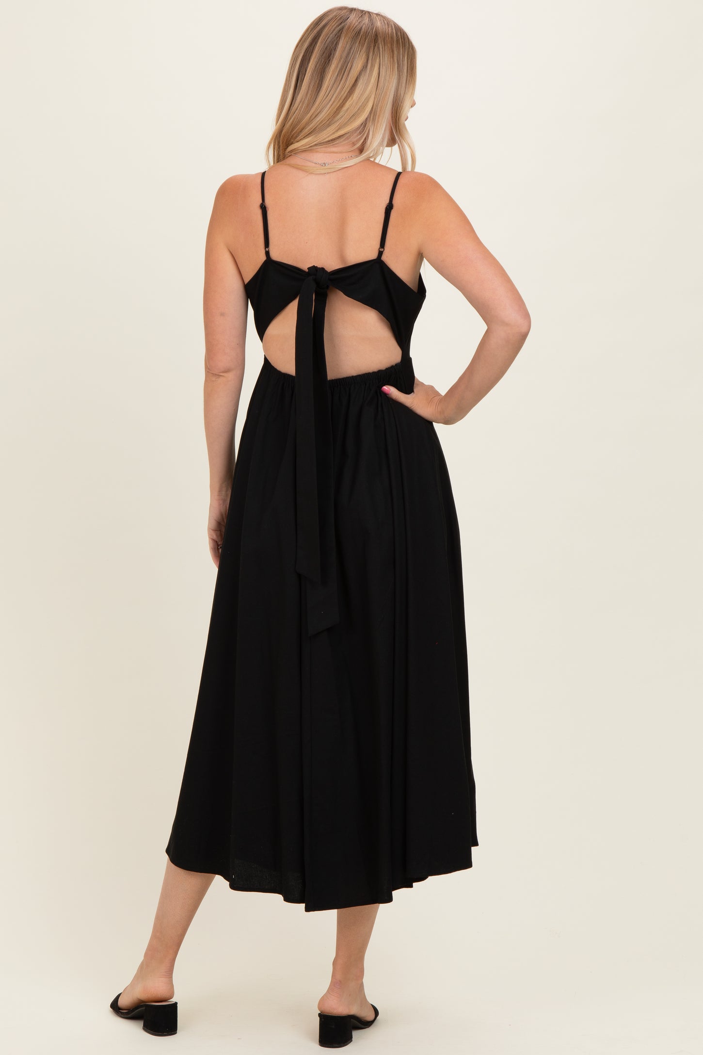 woman wearing a black midi dress with a tie-back detail and spaghetti straps, showing a bare back