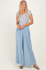 woman wearing a gray short sleeve henley top and light blue wide leg pants standing against a neutral background