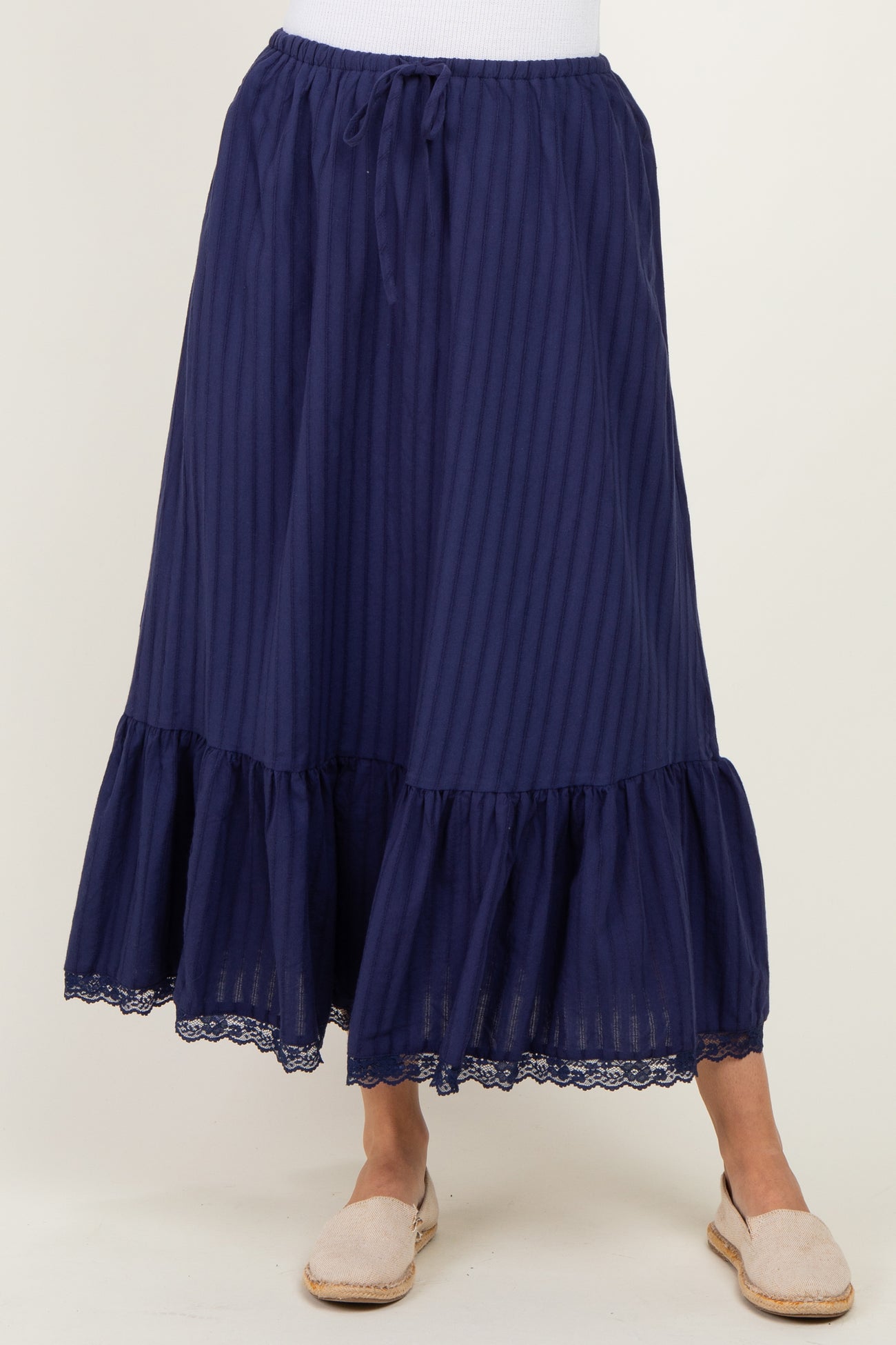 woman wearing a navy blue maxi skirt with vertical stripes and a layered lace trim at the hem