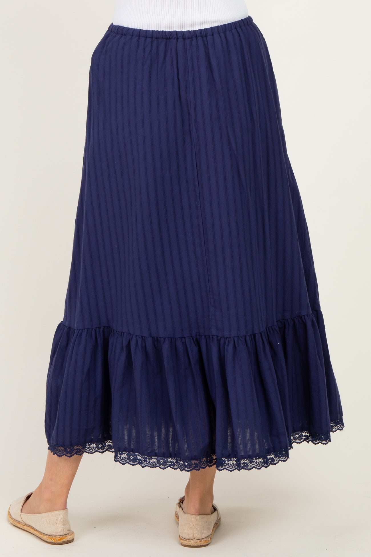 woman wearing a navy blue striped maxi skirt with a ruffle hem and lace trim, showcased from the back