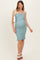 woman wearing a light blue smocked maternity dress with ruffle hem and holding a white bag, showcasing her baby bump