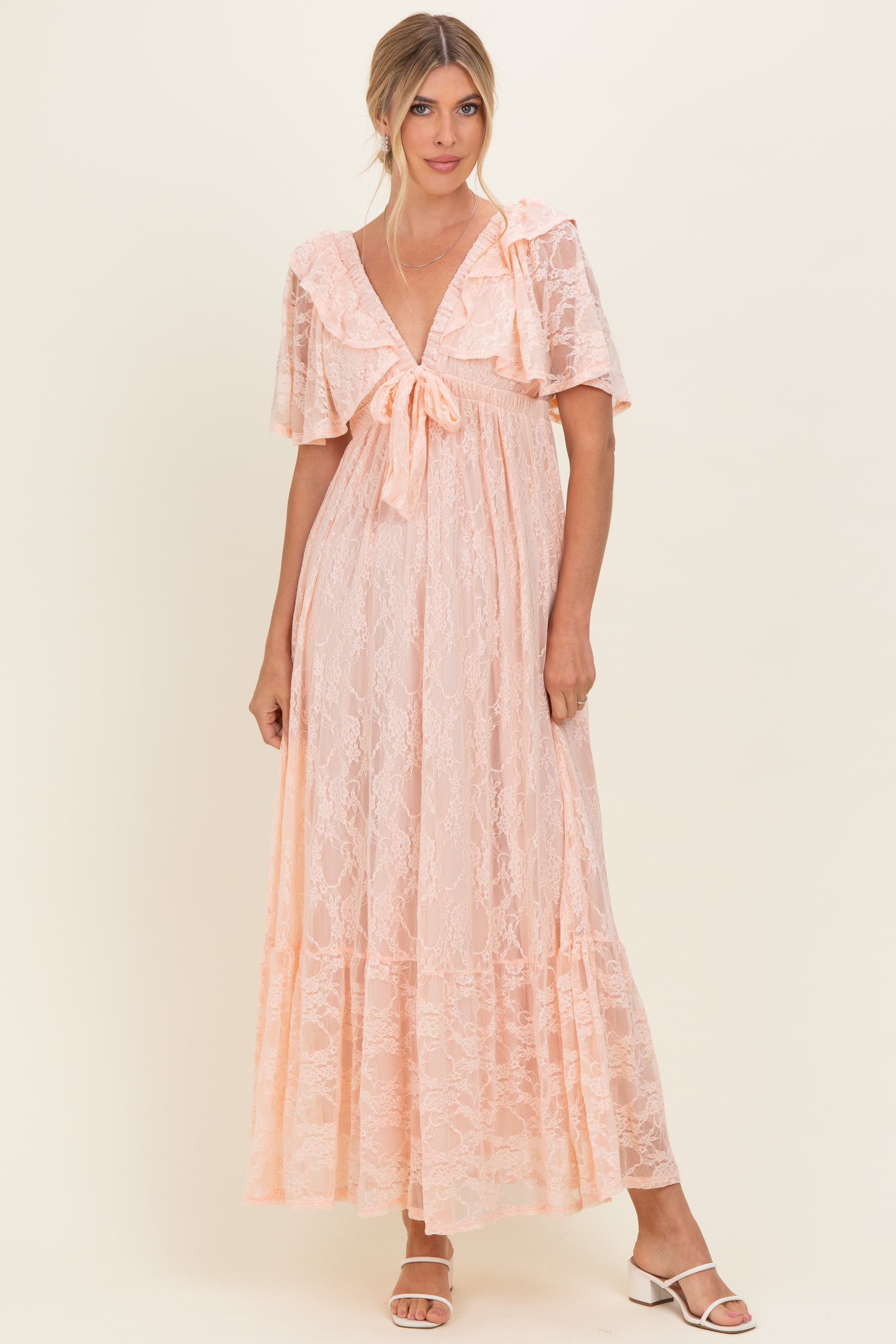 woman wearing a light peach maxi dress with lace detailing, short sleeves, and a bow tie at the waist