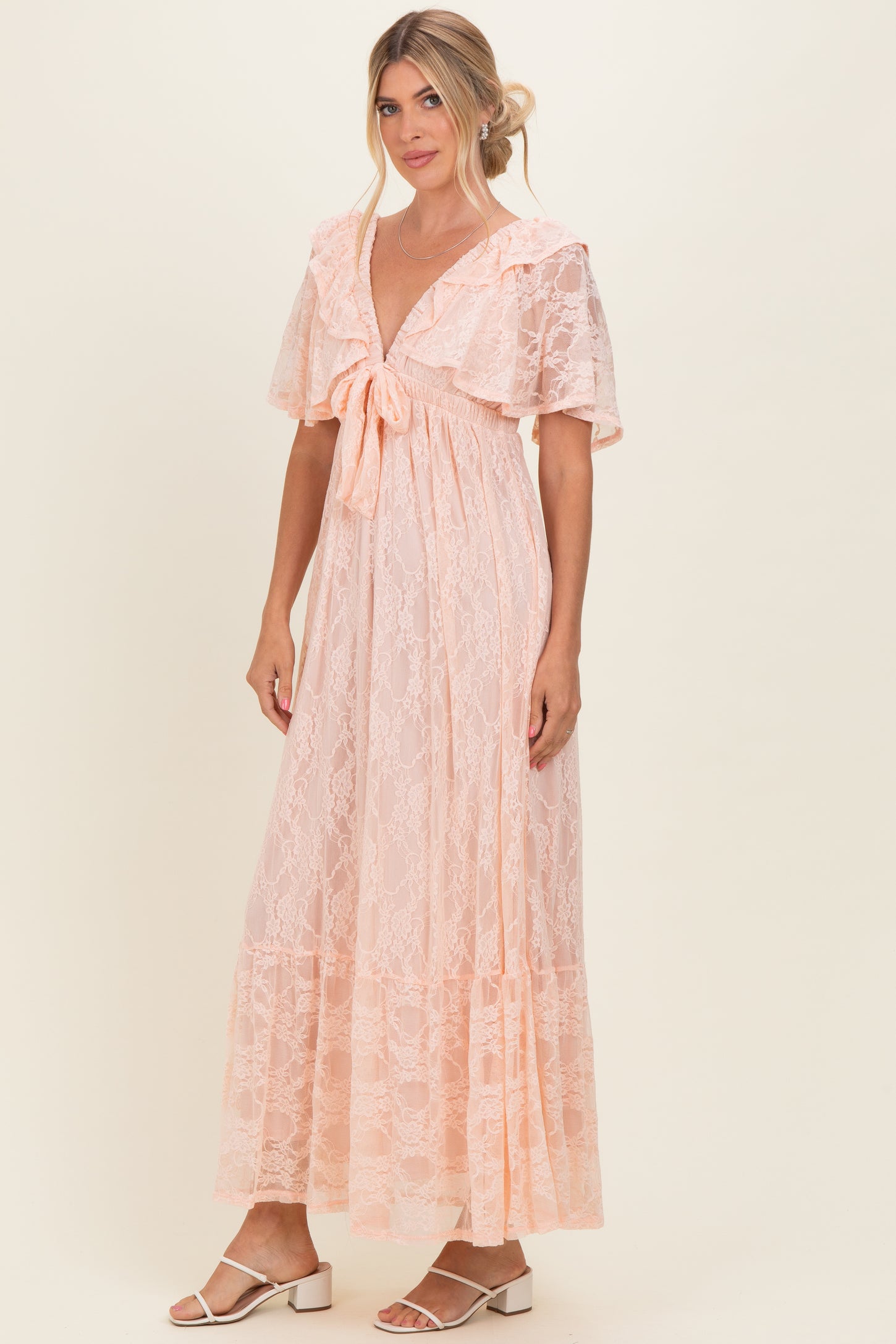 woman wearing a light pink lace maxi dress with flutter sleeves and a tie front detail