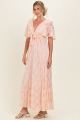 woman wearing a light pink lace maxi dress with flutter sleeves and a tie front detail