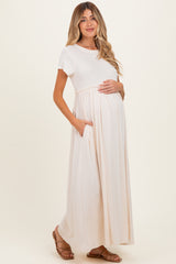 woman wearing a light beige maternity maxi dress with short sleeves and side pockets, showing her baby bump